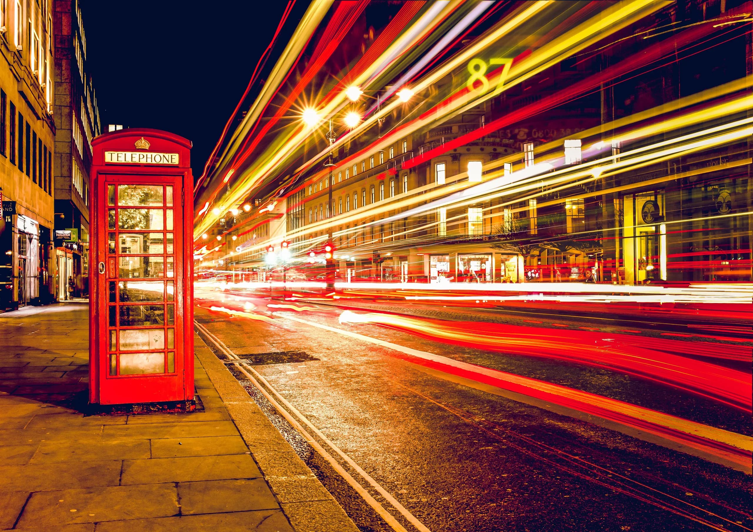 Red London telephone box beside city traffic light trails at night